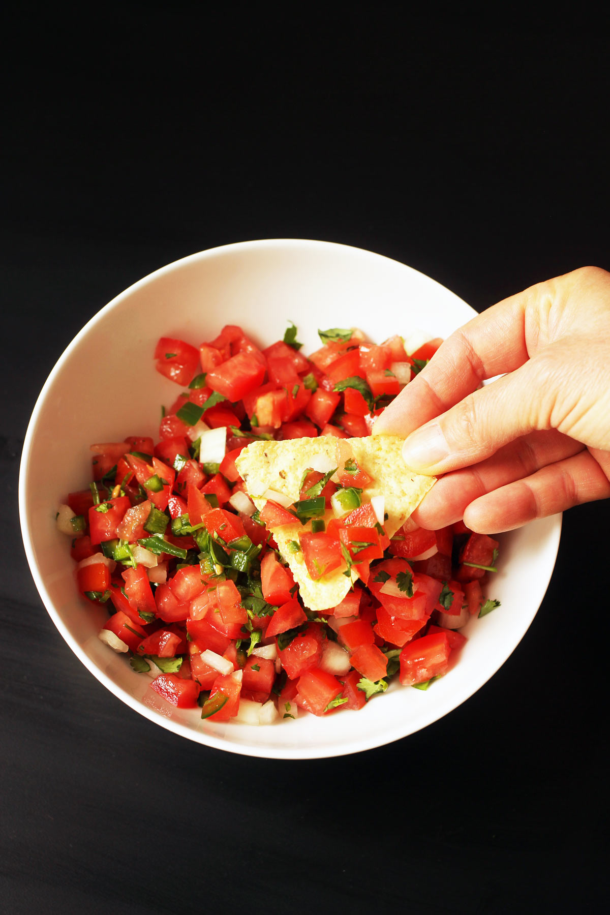 dipping chip in white bowl of pico de gallo.