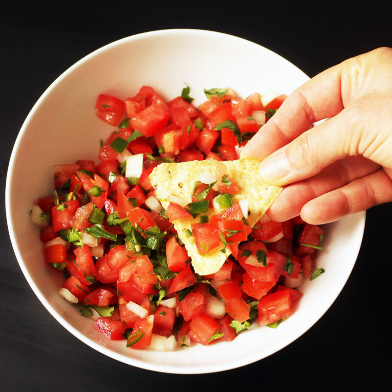 hand dipping chip into bowl of pico de gallo.