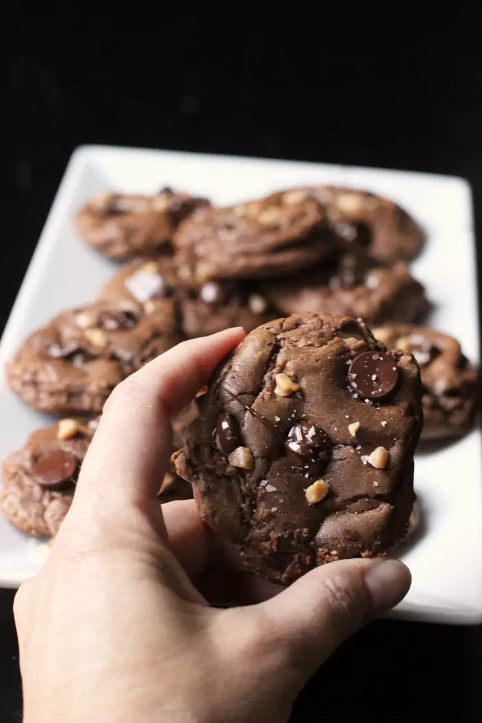 hand holding chocolate cookie in front of platter