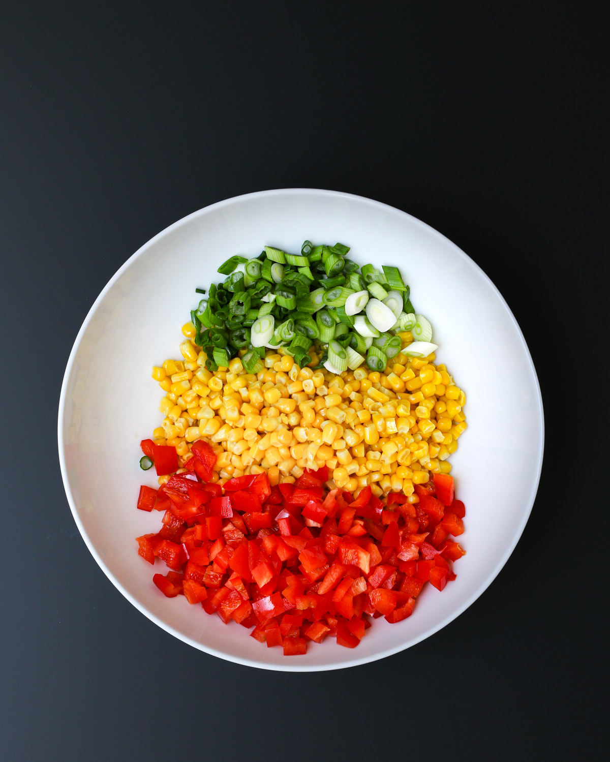 green onion, corn kernels, and diced red pepper in white mixing bowl.