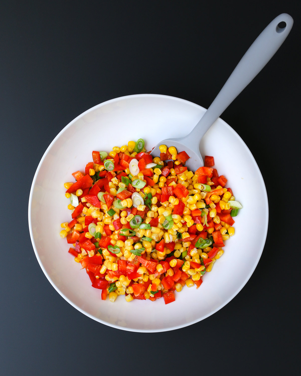 gray spatula submerged into the mixture of vegetables in the bowl.
