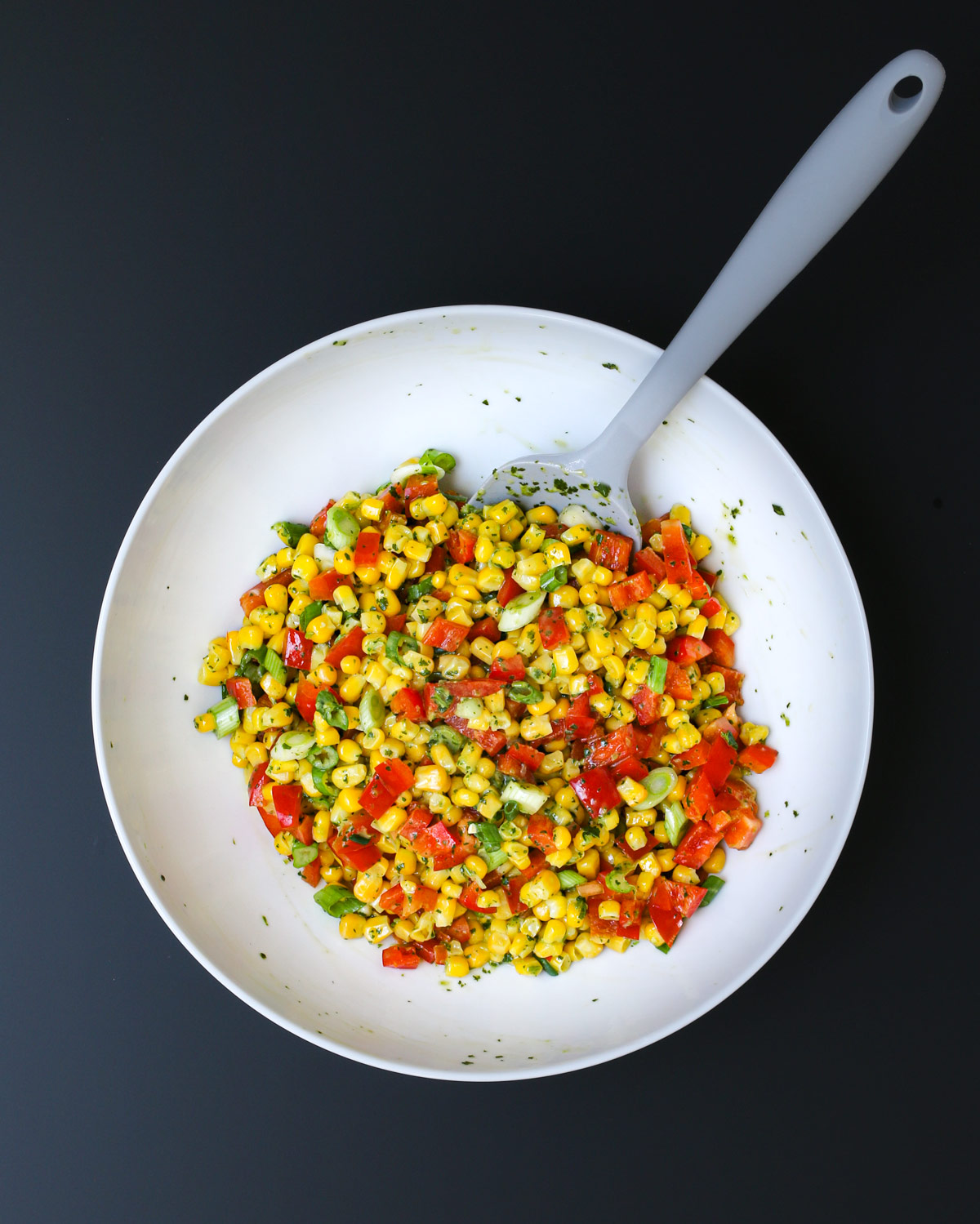 gray spatula submerged in the mixed corn salad in the bowl.