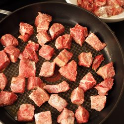 adding floured beef cubes to skillet for browning
