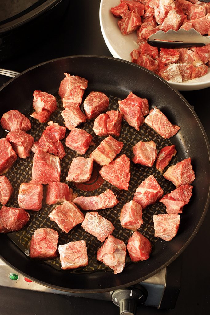 adding floured beef cubes to skillet for browning
