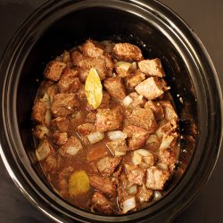 beef cubes broth and bay leaf in slow cooker crock