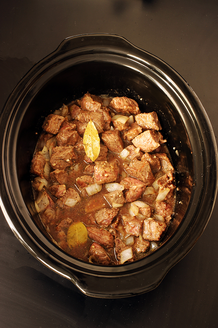 beef cubes broth and bay leaf in slow cooker crock