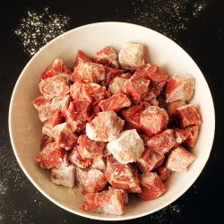 floured beef cubes in white bowl on black table