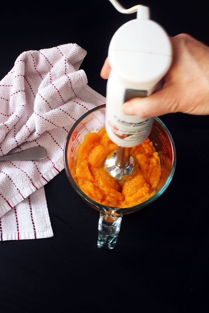 holding immersion blender to blend squash in bowl