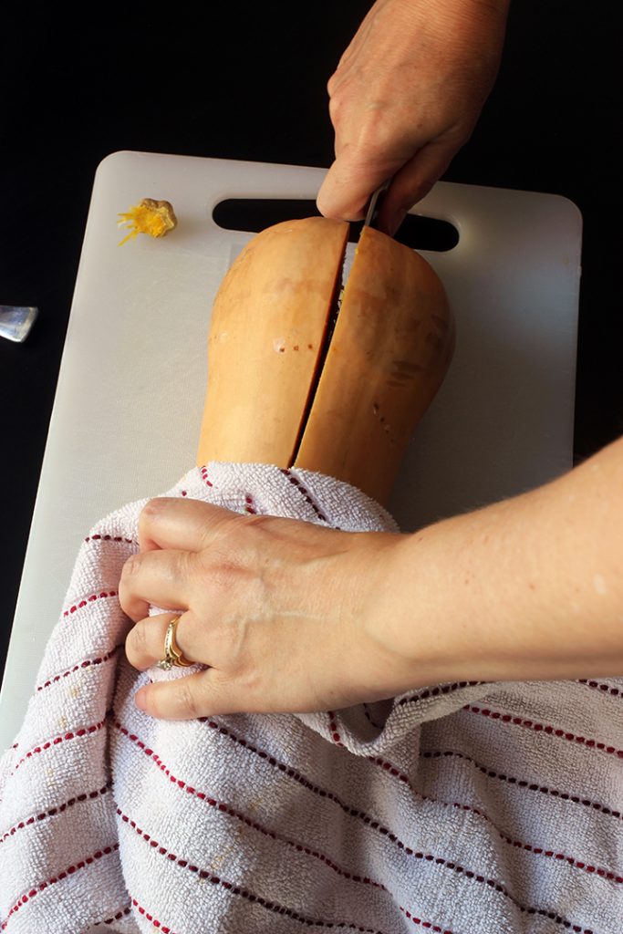 A close up of a hand slicing squash in half