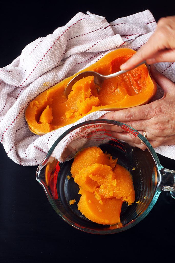 hand scooping out flesh of cooked Squash