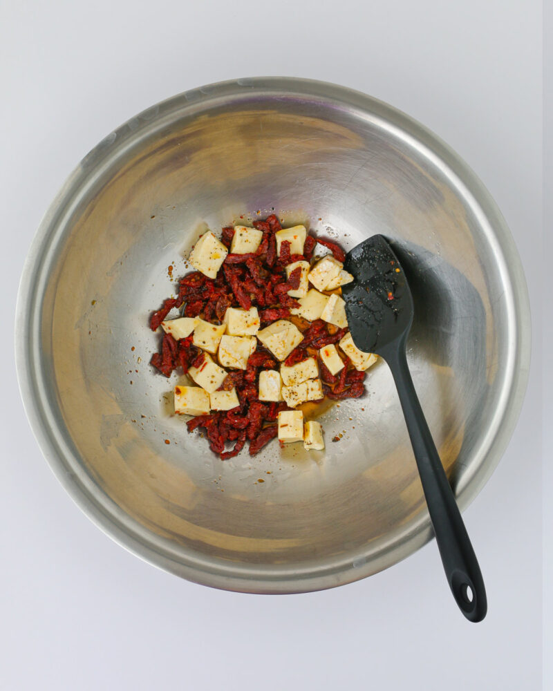 cheese and tomatoes in bowl stirred with a spatula.