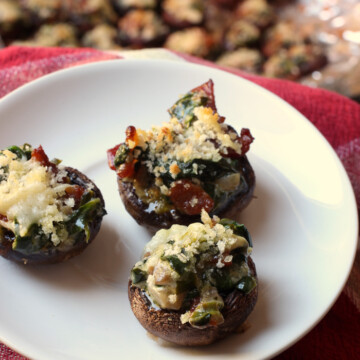 three stuffed mushrooms on plate with platter of mushrooms in background