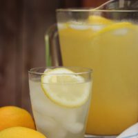 A pitcher of Lemonade on a table with lemons