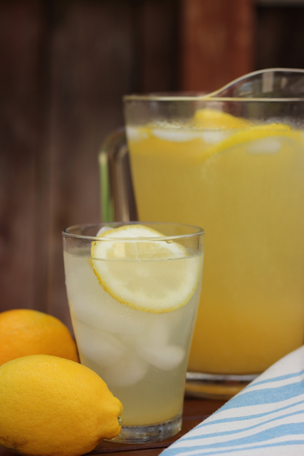 A pitcher of Lemonade on a table with lemons