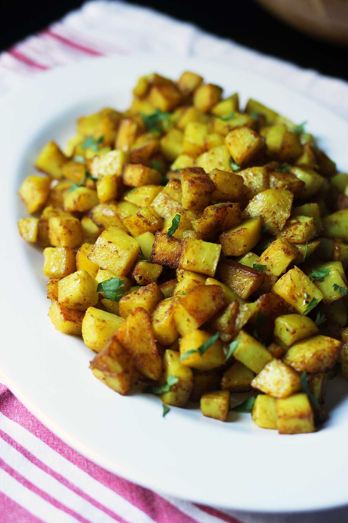 white oval platter of curried potatoes on a red striped cloth.