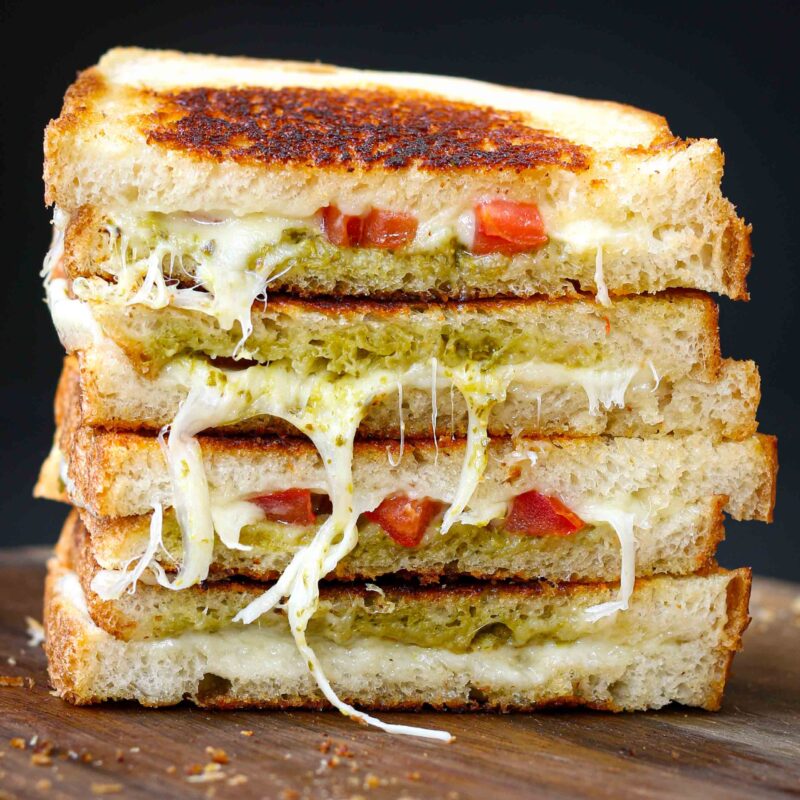 close up of cut side of two sandwiches stacked with cheese pulls and pesto showing.