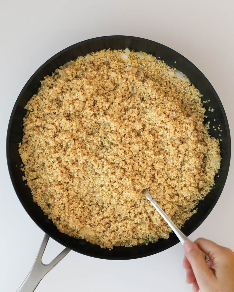 fluffing the cooked quinoa pilaf with a fork.