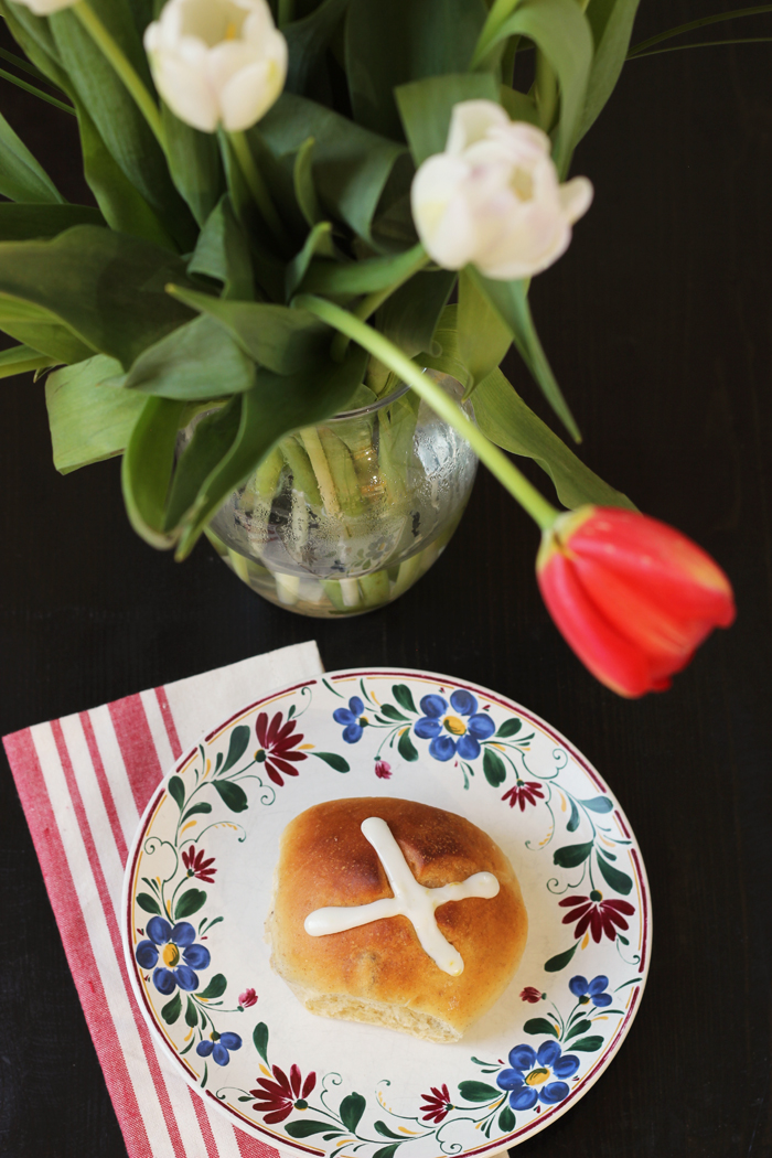 hot cross bun on a plate next to vase of flowers