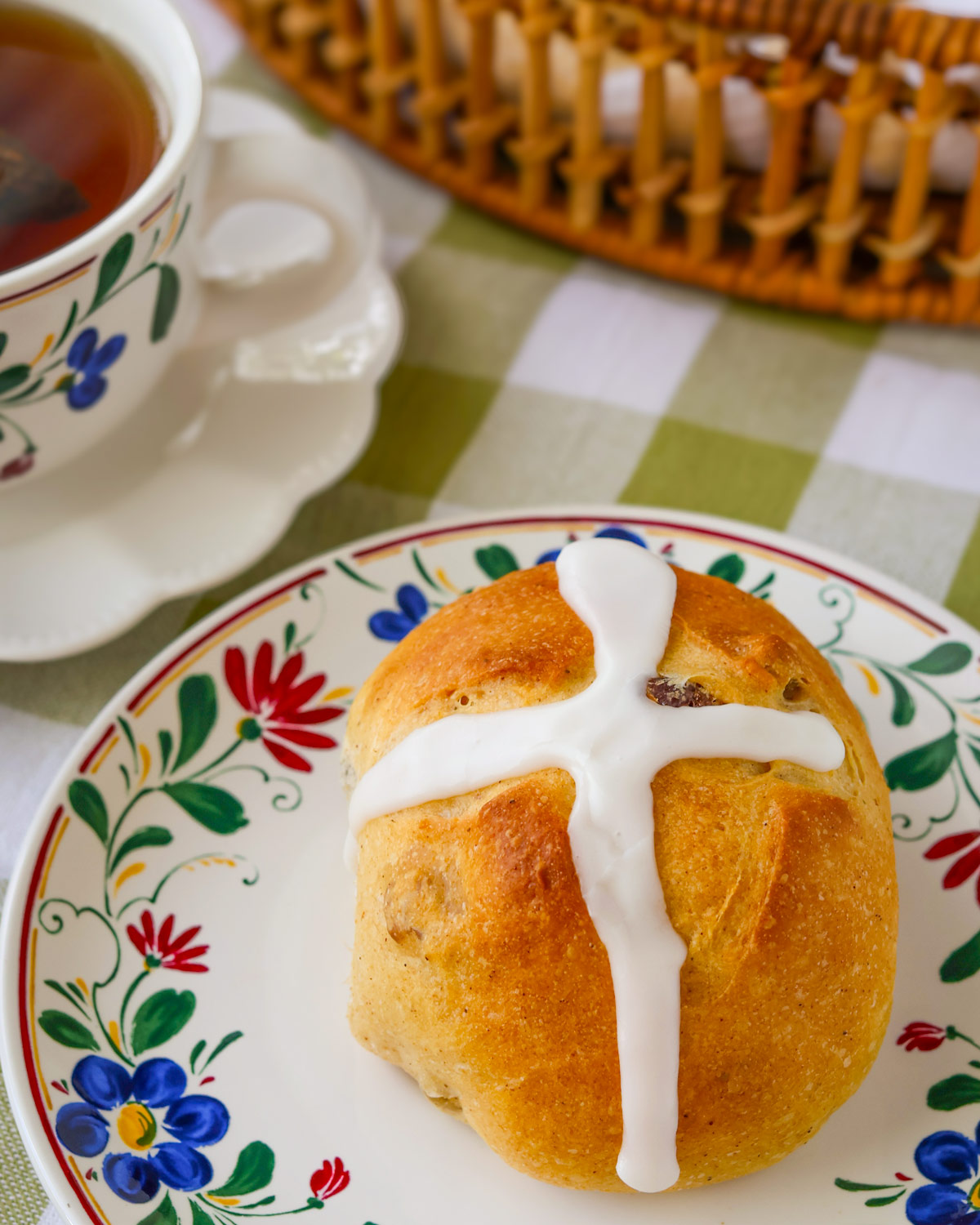 hot cross bun on flowered plate next to a cup of tea.