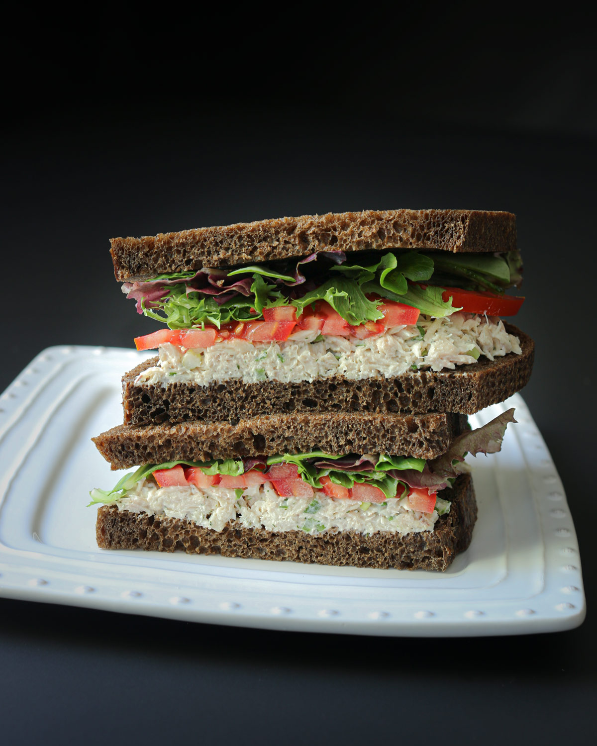 halves of tuna sandwich on pumpernickel bread, cut and stacked on a plate.