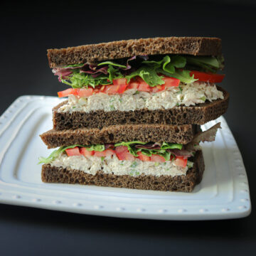 two halves of a tuna sandwich, stacked on a white plate, cut side facing the camera.