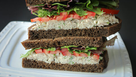 two halves of a tuna sandwich, stacked on a white plate, cut side facing the camera.