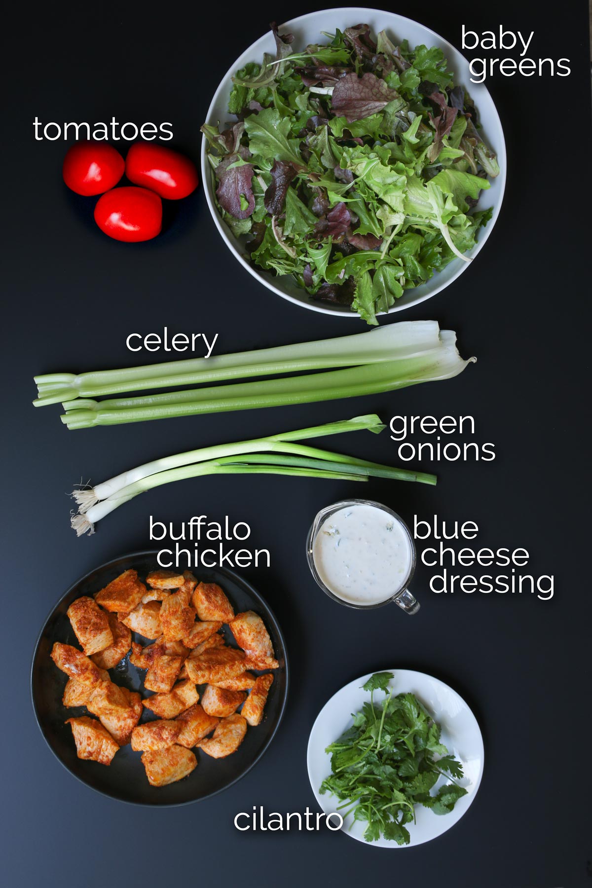 ingredients for buffalo chicken salad laid out on black table.