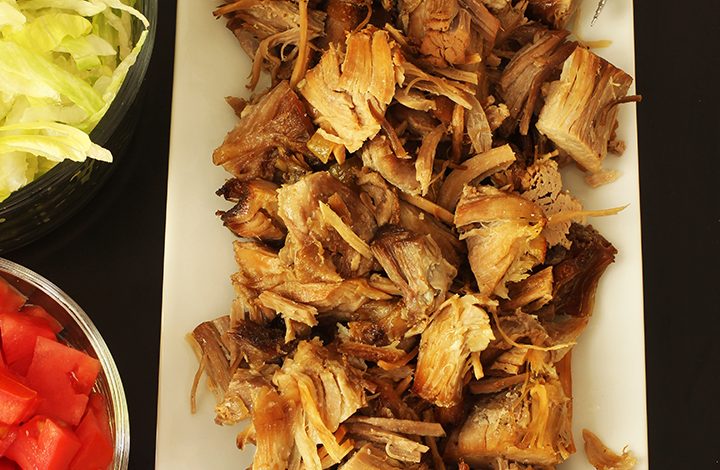 carnitas on platter next to bowls of tomatoes and lettuce