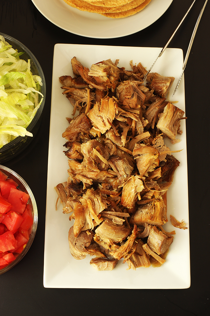 carnitas on platter next to bowls of tomatoes and lettuce