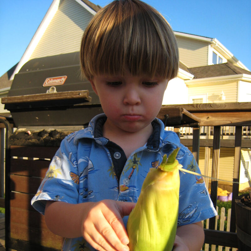toddler boy with ear of corn on deck.