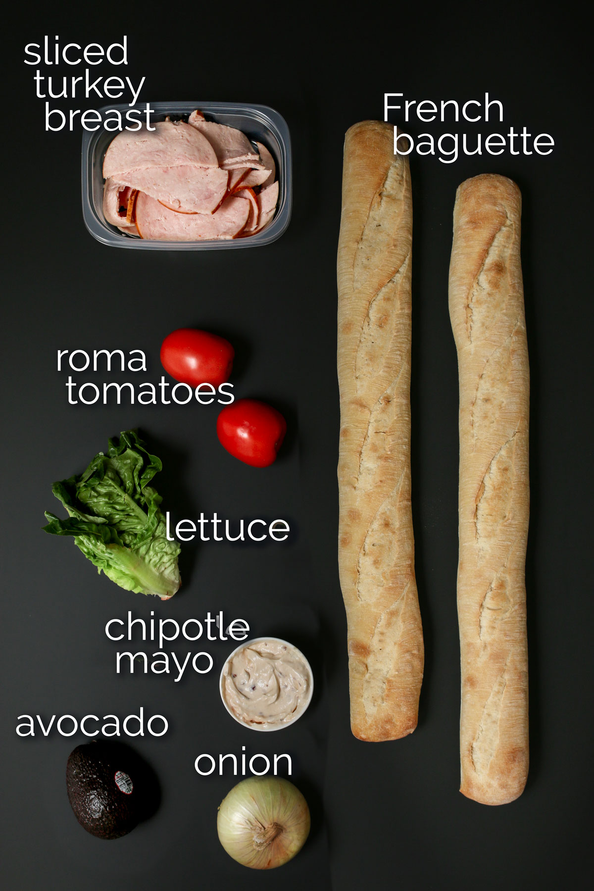 ingredients for turkey baguette sandwiches laid out on a black table.