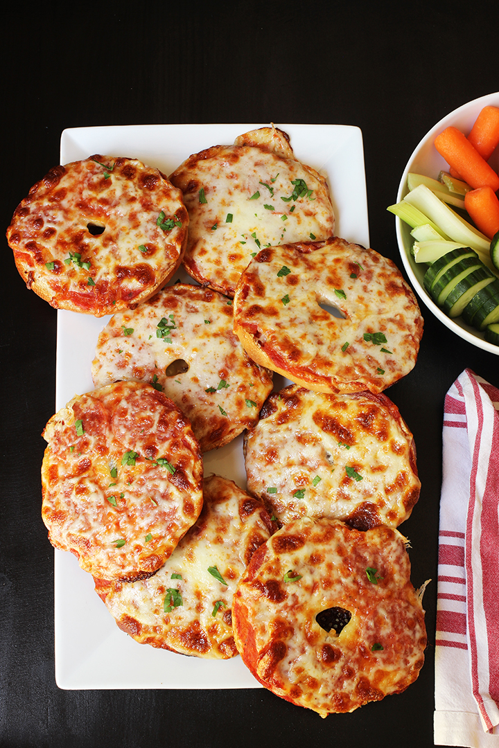 white tray of pizza bagels with red striped cloth and veggie tray