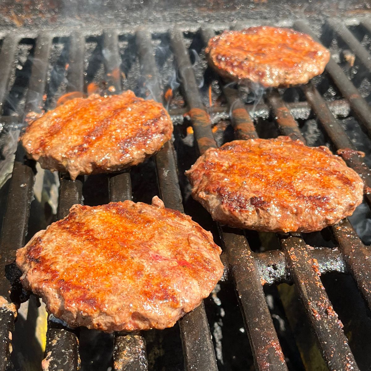 four burgers with char marks on a hot outdoor gas grill.