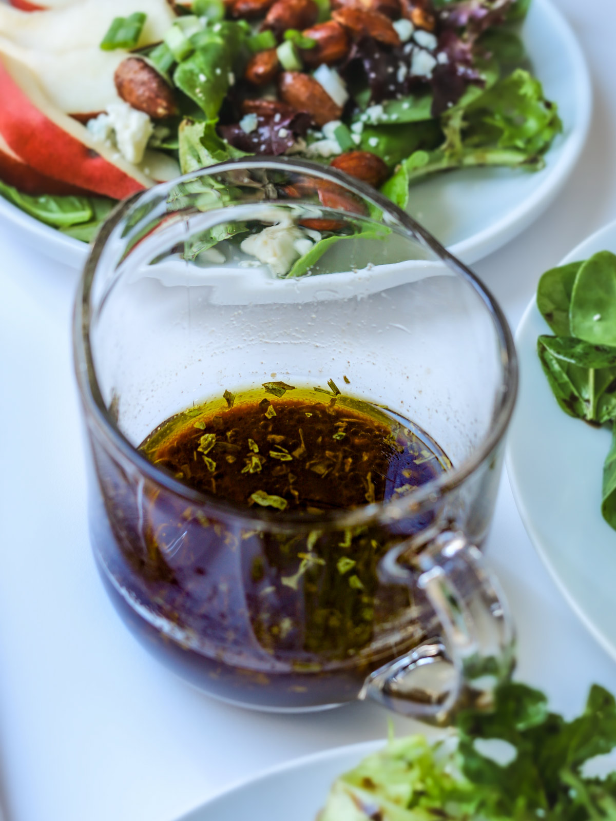 small glass pitcher of balsamic vinaigrette near plates of salad.