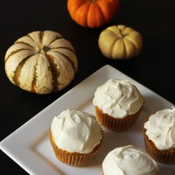 four cupcakes on plate on black table with pumpkins