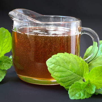 sideview of pitcher of peppermint syrup with fresh mint leaves.