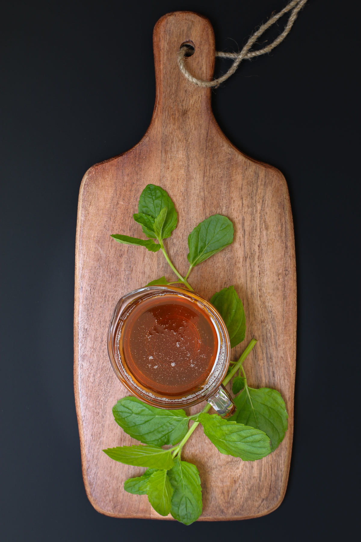 small glass pitcher of mint syrup on wood board with sprigs of fresh mint.