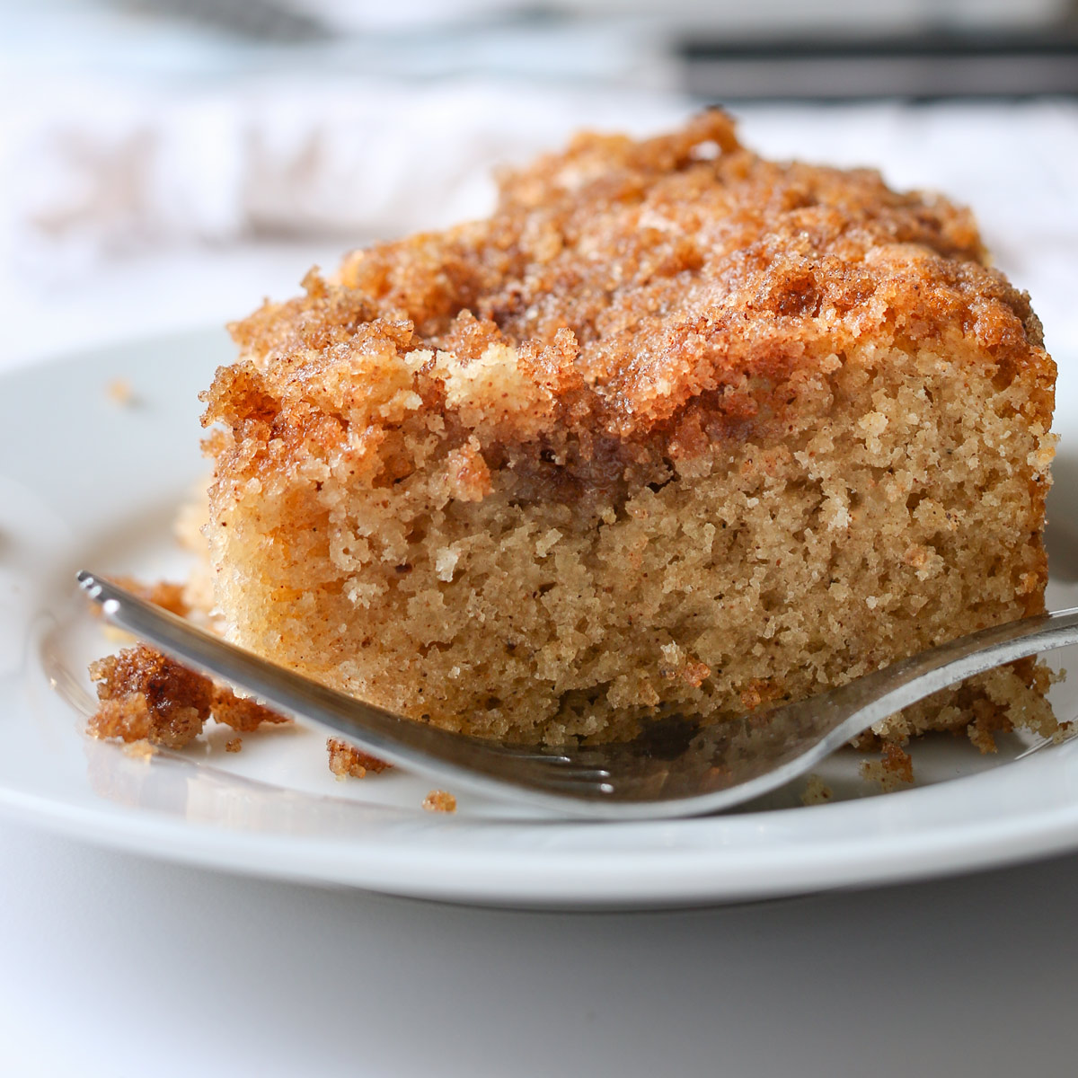 close up of square of cinnamon coffee cake on white plate with fork.