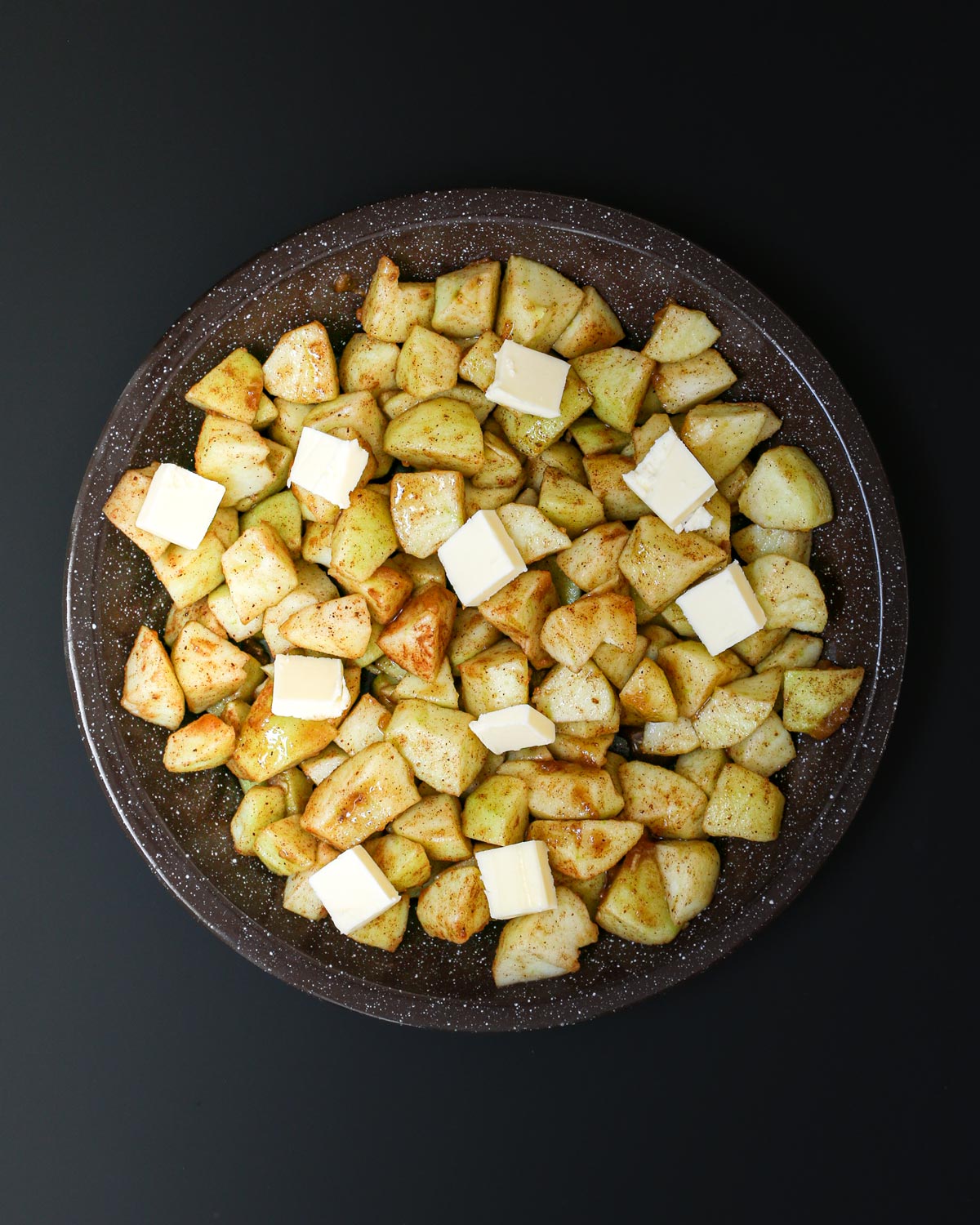 apple mixture in a brown pie plate dotted with small cubes of butter.