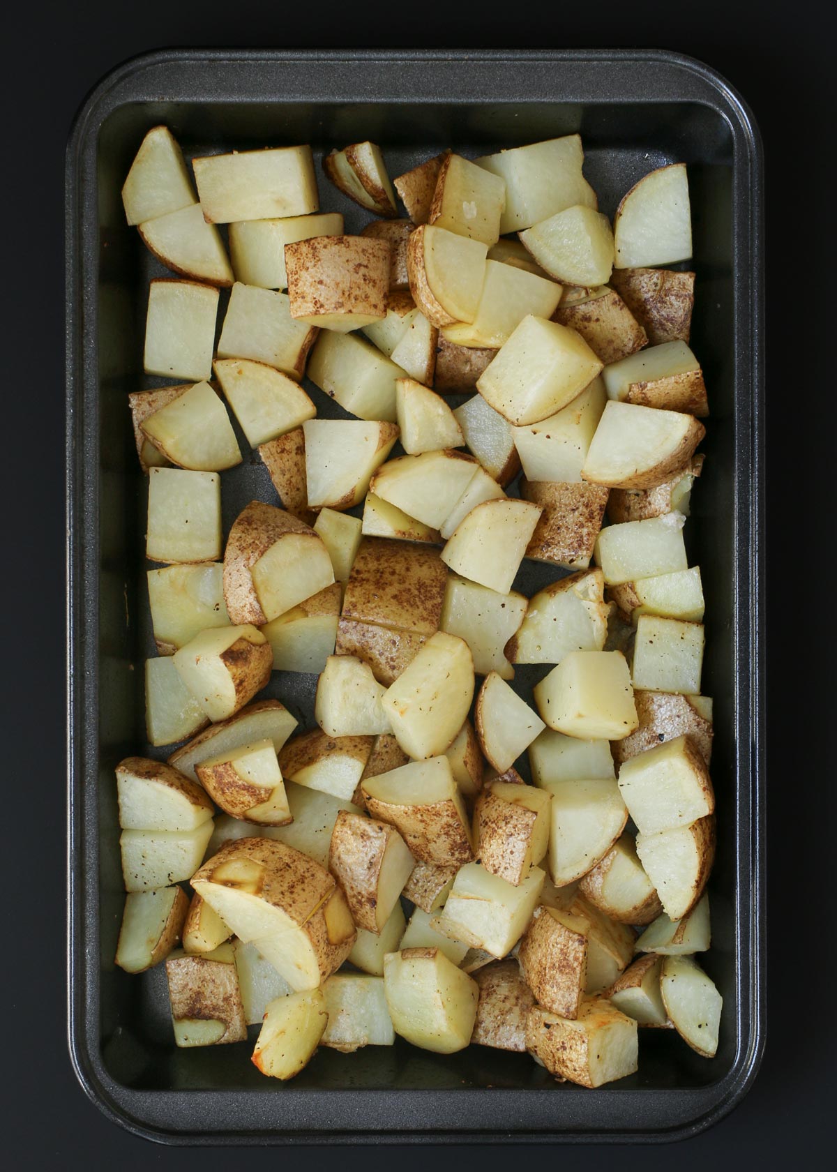 cooked potato cubes laid out in small baking pan.