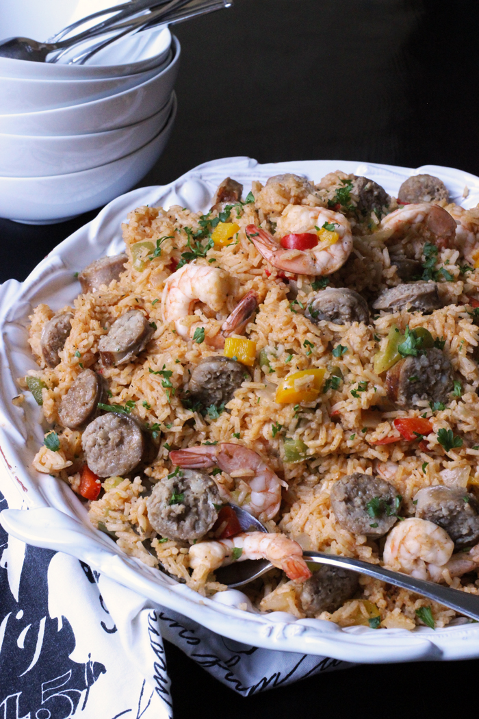 white platter of jambalaya next to stack of white bowls and spoons