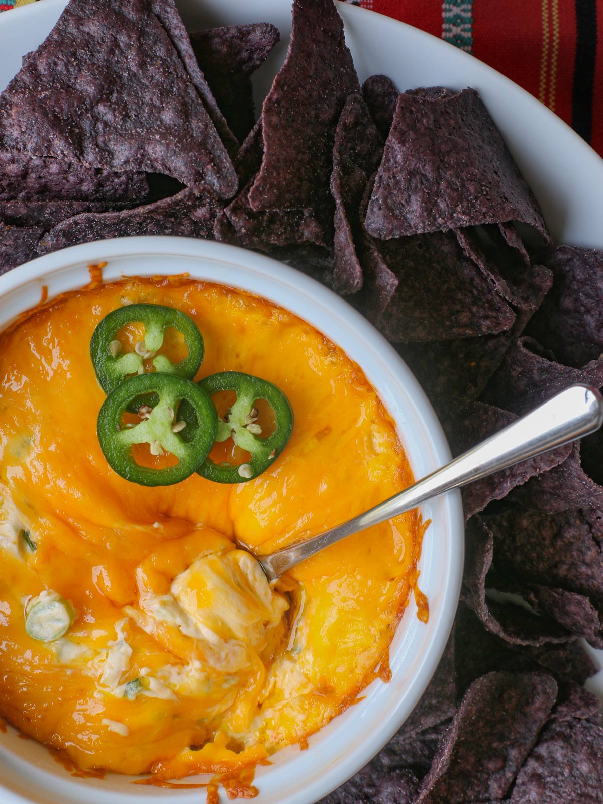 jalapeno cream cheese dip in small white bowl surrounded by blue corn tortilla chips.