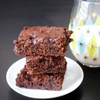 stack of brownies on white plate next to glass of milk