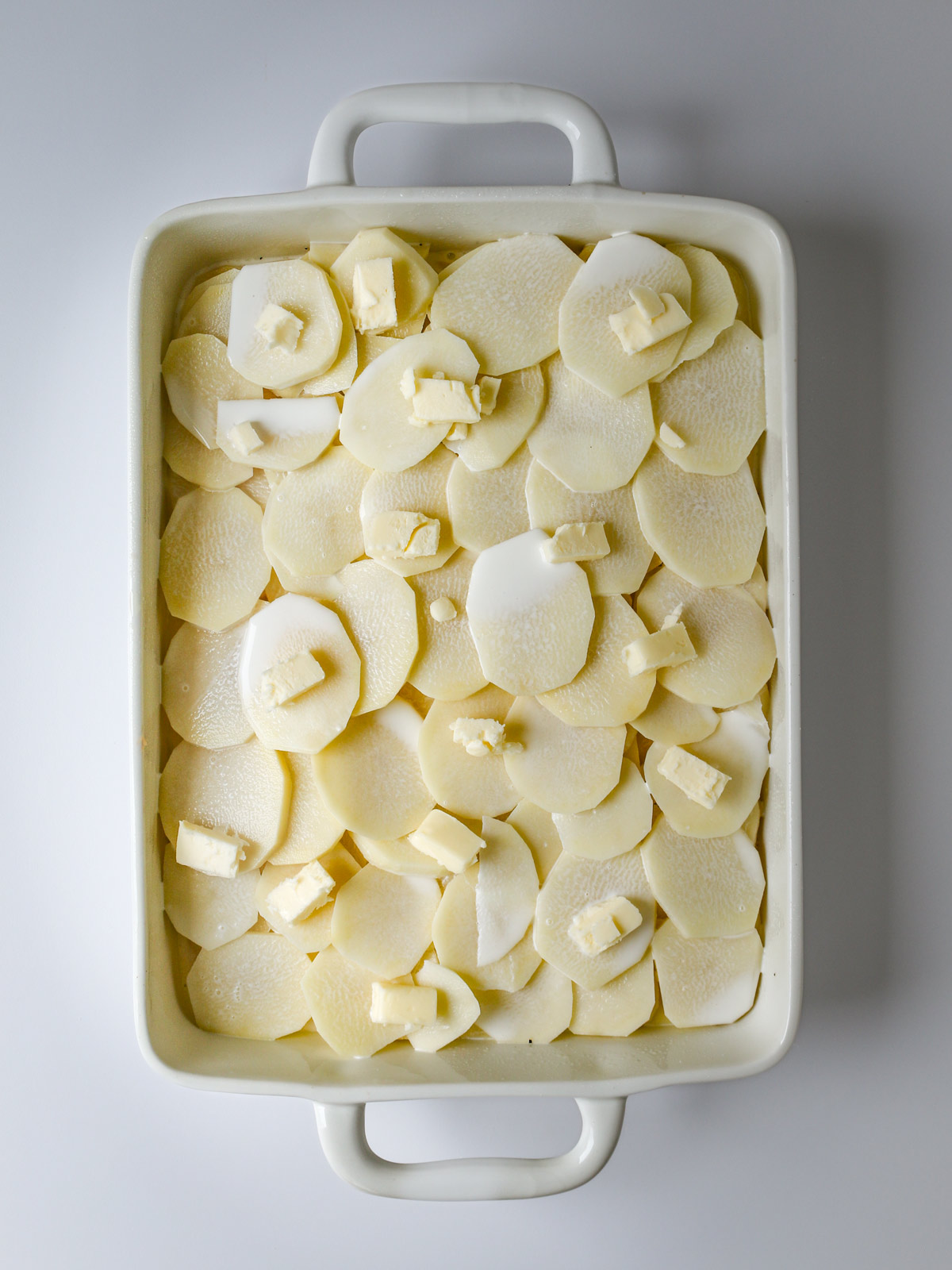 pats of butter laid over potatoes and half and half in baking dish.