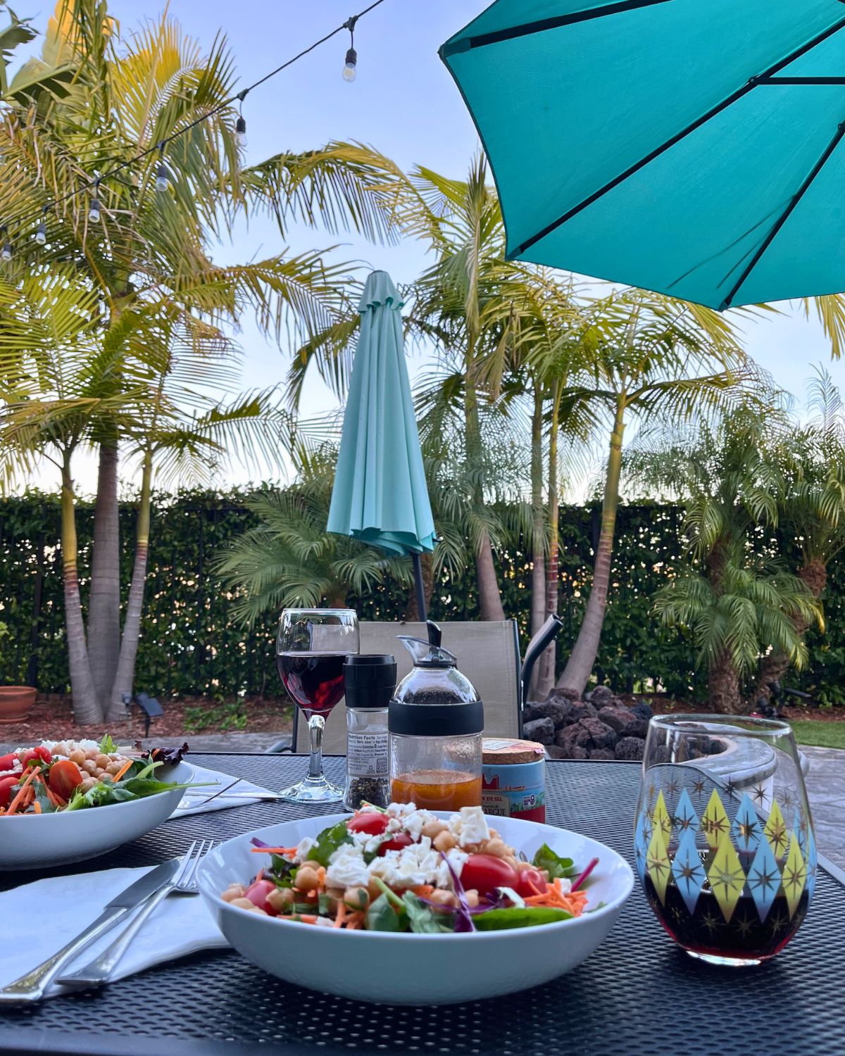 table set on patio with wine glasses and salads, with patio umbrellas in background.