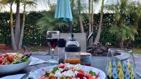 outdoor table set with dinner plates and wine glasses with patio umbrella in background.