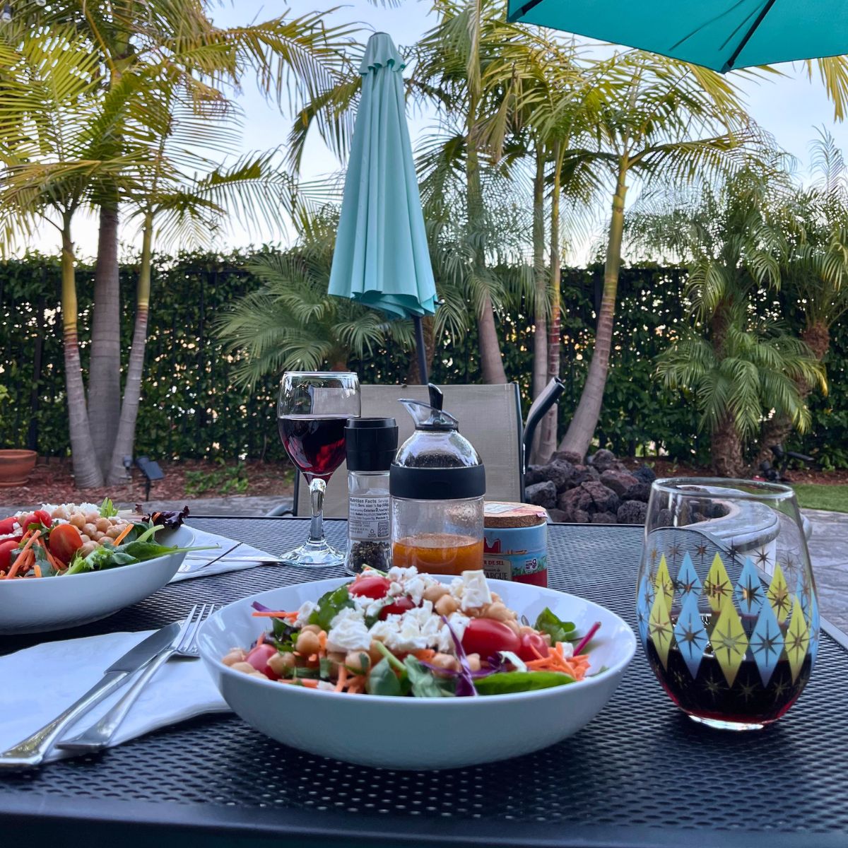 outdoor table set with dinner plates and wine glasses with patio umbrella in background.