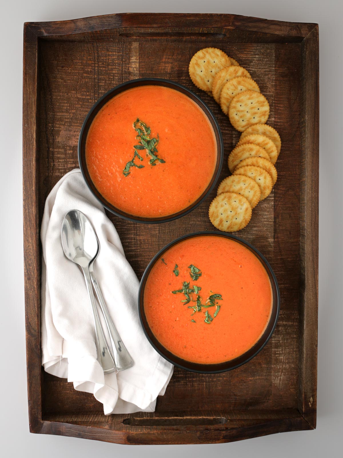 wooden tray of bowls of tomato soup with crackers and spoons.