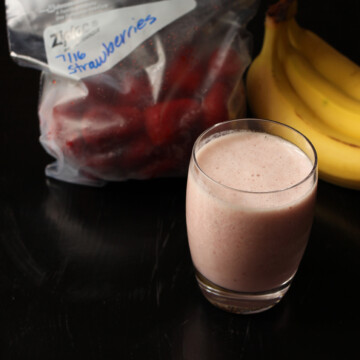 red banana smoothie with strawberries and bunch of bananas