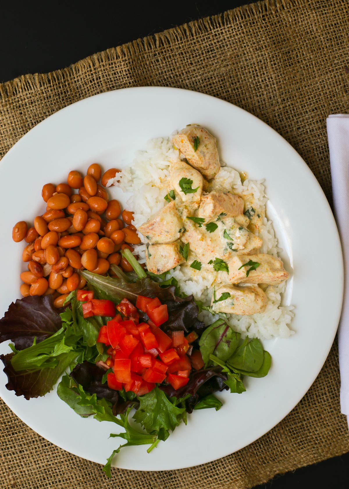 white dinner plate with salad, pinto beans, rice, and sour cream chicken.